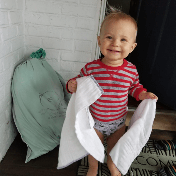 A baby holding cloth diapers from a Green Diaper Babies delivery.